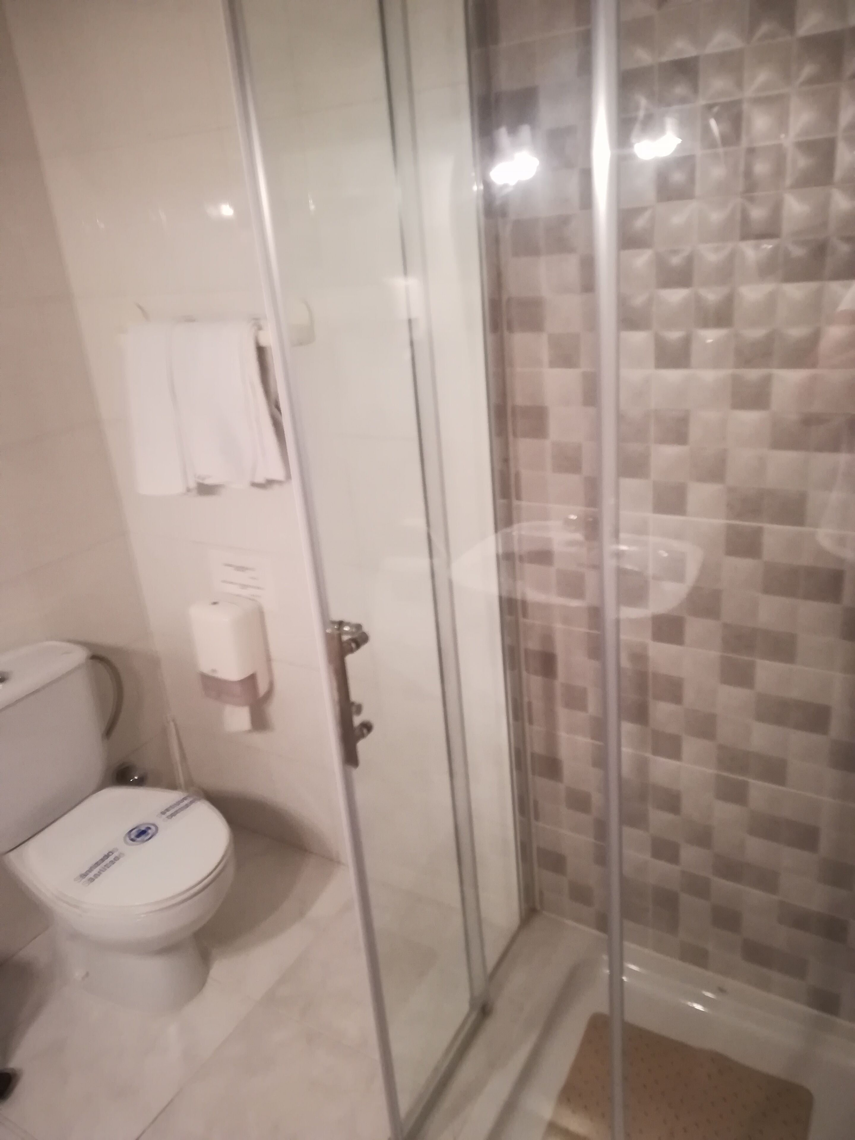 Baño con cabina de ducha de vidrio, inodoro y secador de manos.
