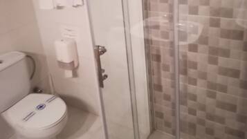 Baño con cabina de ducha de vidrio, inodoro y secador de manos.