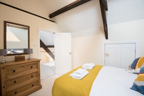 Um quarto com cama, penteadeira, espelho e porta que dá para uma escadaria.