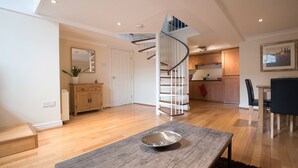 A spacious living area with a wooden floor, a dining table with a metal bowl, a spiral staircase, and a kitchen in the background. - St Andrews Court (Durham)