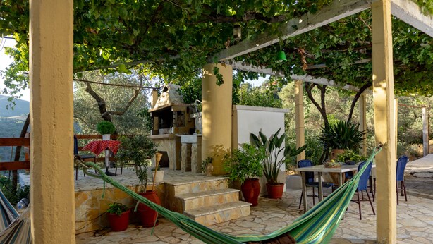 Un patio cubierto con una hamaca, plantas en macetas, una mesa y sillas.
