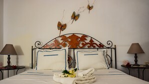 Una cama bien hecha con sábanas blancas y detalles azules, dos mesitas de noche con lámparas, y mariposas decorativas en la pared.