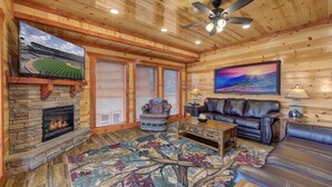 A cozy living room with a stone fireplace, leather sofa, and a large rug. - Mountain Moonshine, Private Indoor Pool, Pool Table, Arcade Game, Theater Room (Sevierville)