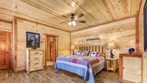 A log cabin bedroom with a bed, dresser, and a ceiling fan. - Mountain Moonshine, Private Indoor Pool, Pool Table, Arcade Game, Theater Room (Sevierville)