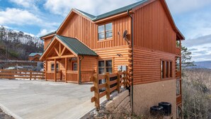 A large log cabin with a welcoming entrance, a covered porch, and a view of the surrounding landscape. - Mountain Moonshine, Private Indoor Pool, Pool Table, Arcade Game, Theater Room (Sevierville)