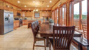 A spacious kitchen with wooden cabinets, a stainless steel refrigerator, and a large dining table with chairs. - Mountain Moonshine, Private Indoor Pool, Pool Table, Arcade Game, Theater Room (Sevierville)