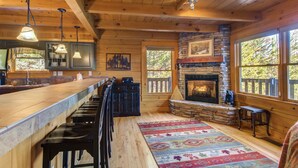 A rustic cabin interior with a long bar, stone fireplace, and large windows. - Tree Top. Beautiful Mountain View, Pool table, Hot Tub, Arcade Game, Private Mountain Setting (Sevierville)