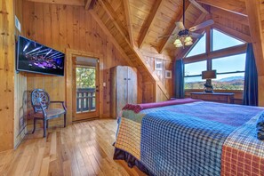A cozy cabin bedroom with a bed, a chair, a TV, and a window with a scenic view. - Tree Top. Beautiful Mountain View, Pool table, Hot Tub, Arcade Game, Private Mountain Setting (Sevierville)