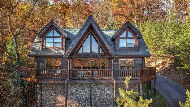 A log cabin with a stone foundation, wooden deck, and multiple windows. - Tree Top. Beautiful Mountain View, Pool table, Hot Tub, Arcade Game, Private Mountain Setting (Sevierville)
