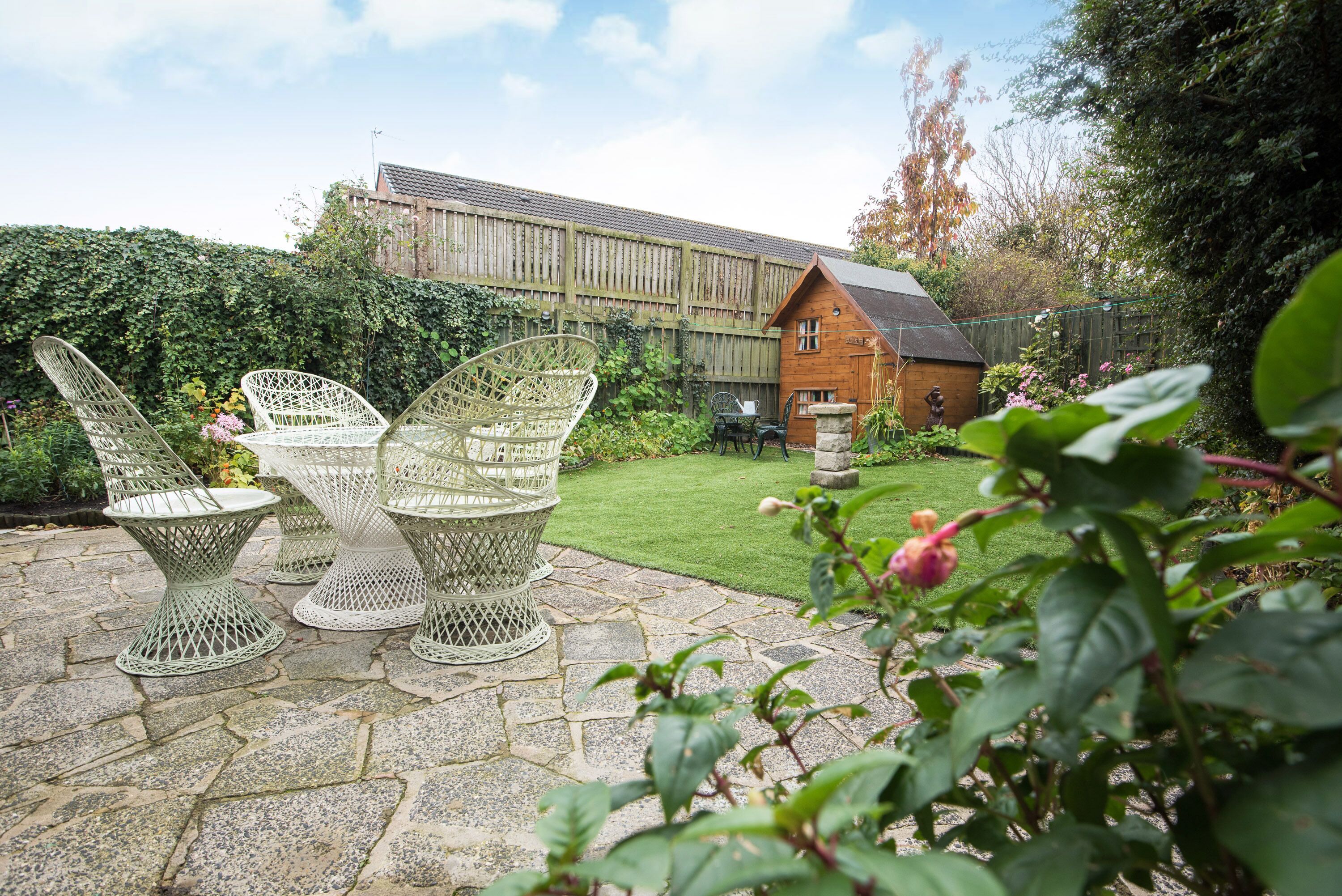 A garden with stone flooring and white metal chairs.