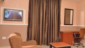 A room with a television, a desk, a chair, and a large window with curtains. - Kelin Court Hotel (Lagos)
