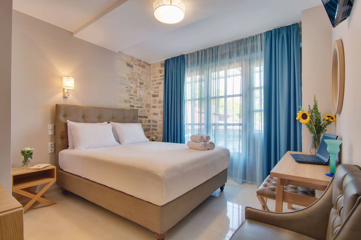 Une chambre d’hôtel avec un grand lit, un bureau avec un ordinateur portable, une chaise et une fenêtre avec des rideaux.