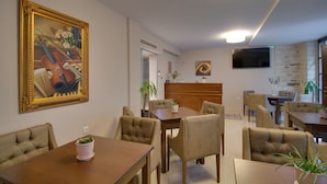 A dining area with a wooden table and chairs, a painting on the wall, and a television mounted on the wall. - Ali Pasha Hotel (Ioannina)