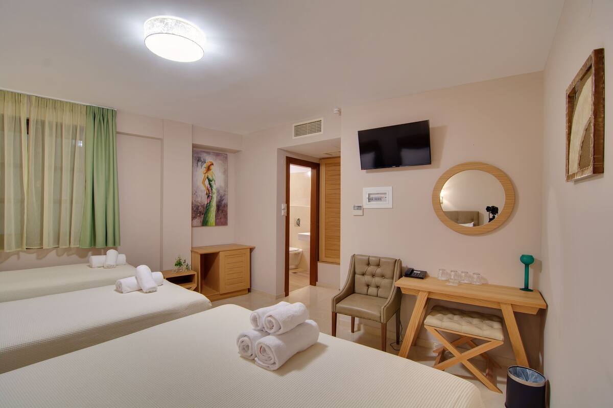 Une chambre d’hôtel avec deux lits, un bureau, une chaise, une télévision et un miroir.