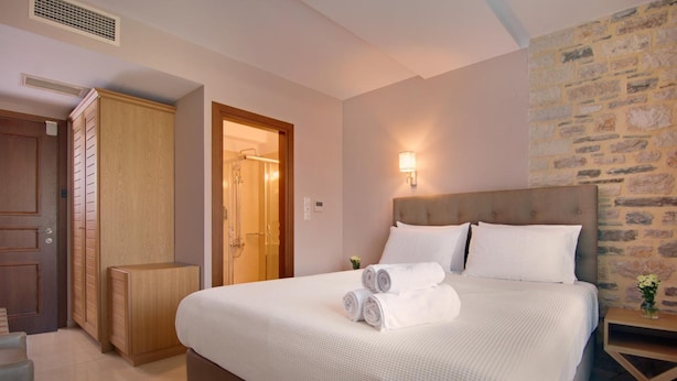 A neatly made bed with rolled towels, a wooden wardrobe, a stone wall, and a nightstand with a lamp. - Ali Pasha Hotel (Ioannina)