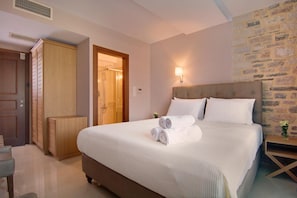 A neatly made bed with rolled towels, a wooden wardrobe, a stone wall, and a nightstand with a lamp. - Ali Pasha Hotel (Ioannina)