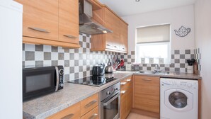 A modern kitchen with wooden cabinets, a microwave, stove, oven, and a washing machine.