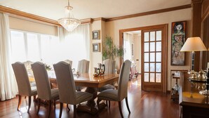 A dining room with a wooden table and chairs, a chandelier, and a large window with curtains. - Spacious villa with private pool and free wifi, sleeps 12 - VILLA NOSTRA (Cambrils)