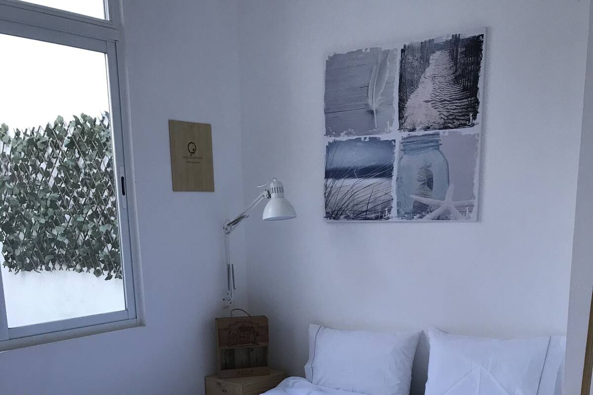 A bedroom with a large bed, white bedding, a nightstand with a lamp, and a window with a view of trees.