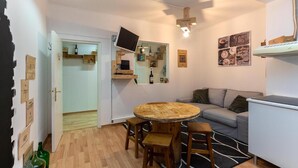 A cozy living room with a round wooden table, a grey sofa, and a television mounted on the wall. - Wine Inn Cascais (Cascais)