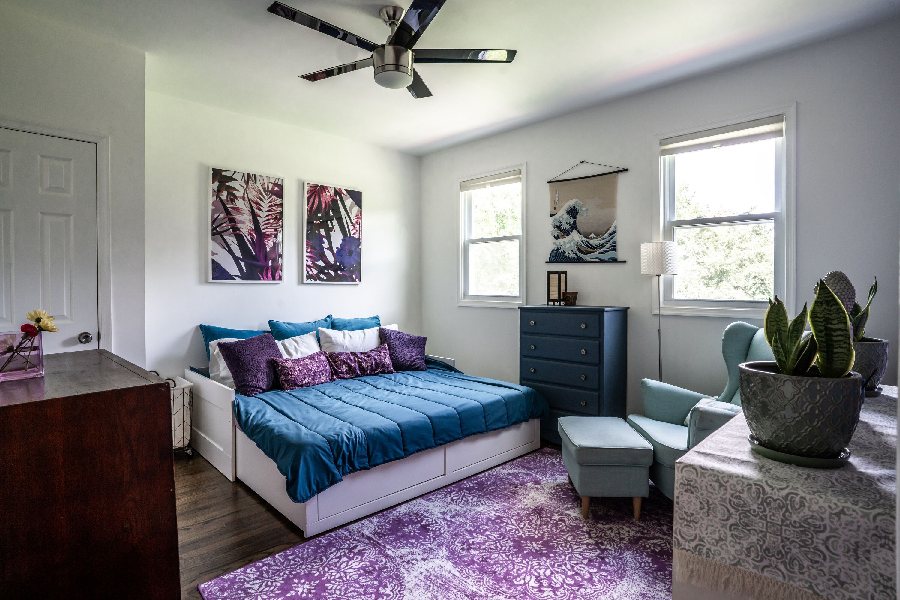 A bedroom with a bed, dresser, chair, and potted plant.