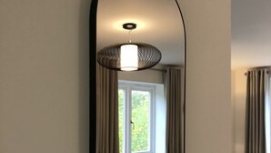 A room with a large oval mirror on the wall, a window with curtains, and a radiator below. - Parkside Penthouse (Yeovil)