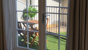 A room with a sliding glass door leading to an outdoor patio with a wooden table and chairs, a small potted plant, and a view of a building in the background. - Parkside Penthouse (Yeovil)
