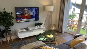A modern living room with a flat-screen TV mounted on the wall, a glass coffee table, a white sofa, and a patterned rug. - Parkside Penthouse (Yeovil)