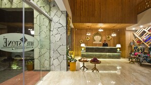 A hotel lobby with a reception desk, a wooden ceiling, and a stone wall. - White Stone Resorts (Manali)