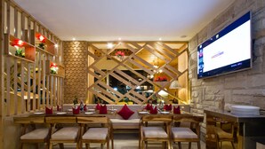 A restaurant with wooden furniture, a stone wall, and a mounted TV screen. - White Stone Resorts (Manali)