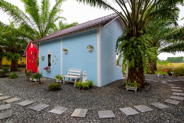 Un pequeño edificio azul claro con una puerta roja, un banco y plantas en macetas.