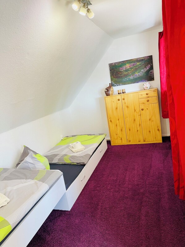 A compact bedroom with a bed, a wooden cabinet, and a painting on the wall.