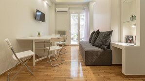 A modern living room with a sofa, a dining table with chairs, a TV mounted on the wall, and a window with curtains. - Cozy Flat with Terrace & Patio near Lycabettus (Athens)