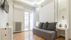 A modern living room with a grey sofa, a white desk, and a glass shelf unit. - Cozy Flat with Terrace & Patio near Lycabettus (Athens)
