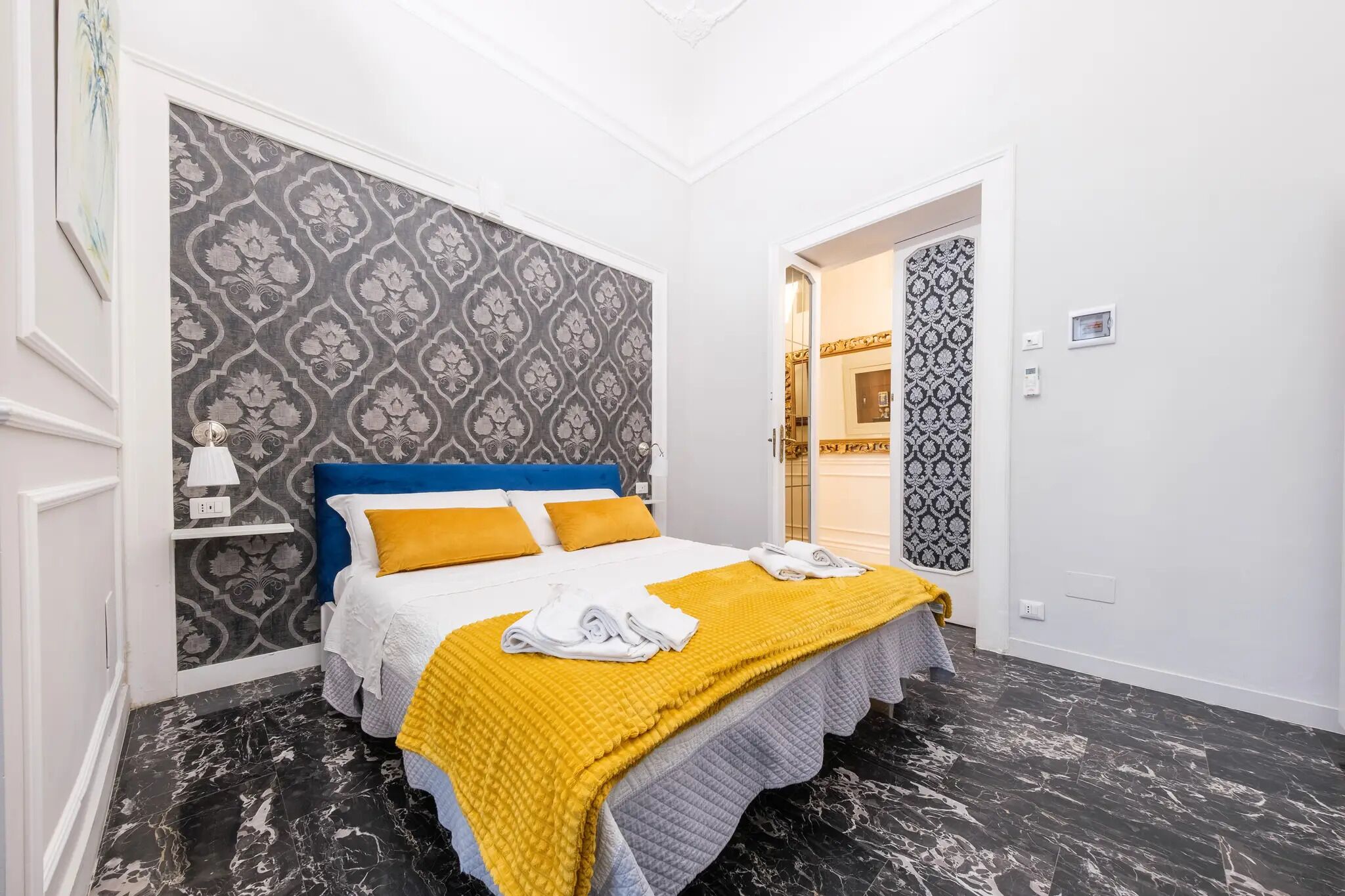 Une chambre à coucher bien rangée, avec un lit, une table de chevet et un mur décoré d’un motif.