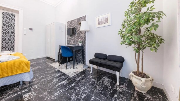 A hotel room with a bed, a desk, a chair, a potted plant, and a bench. - B&B Il Galleone (Messina)