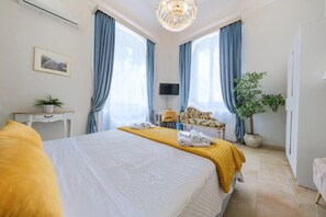 Una habitación de hotel con una cama grande, un escritorio, una silla, un televisor y una planta en maceta.