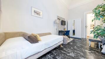 A bedroom with a bed, a desk, a chair, a TV, and a plant.