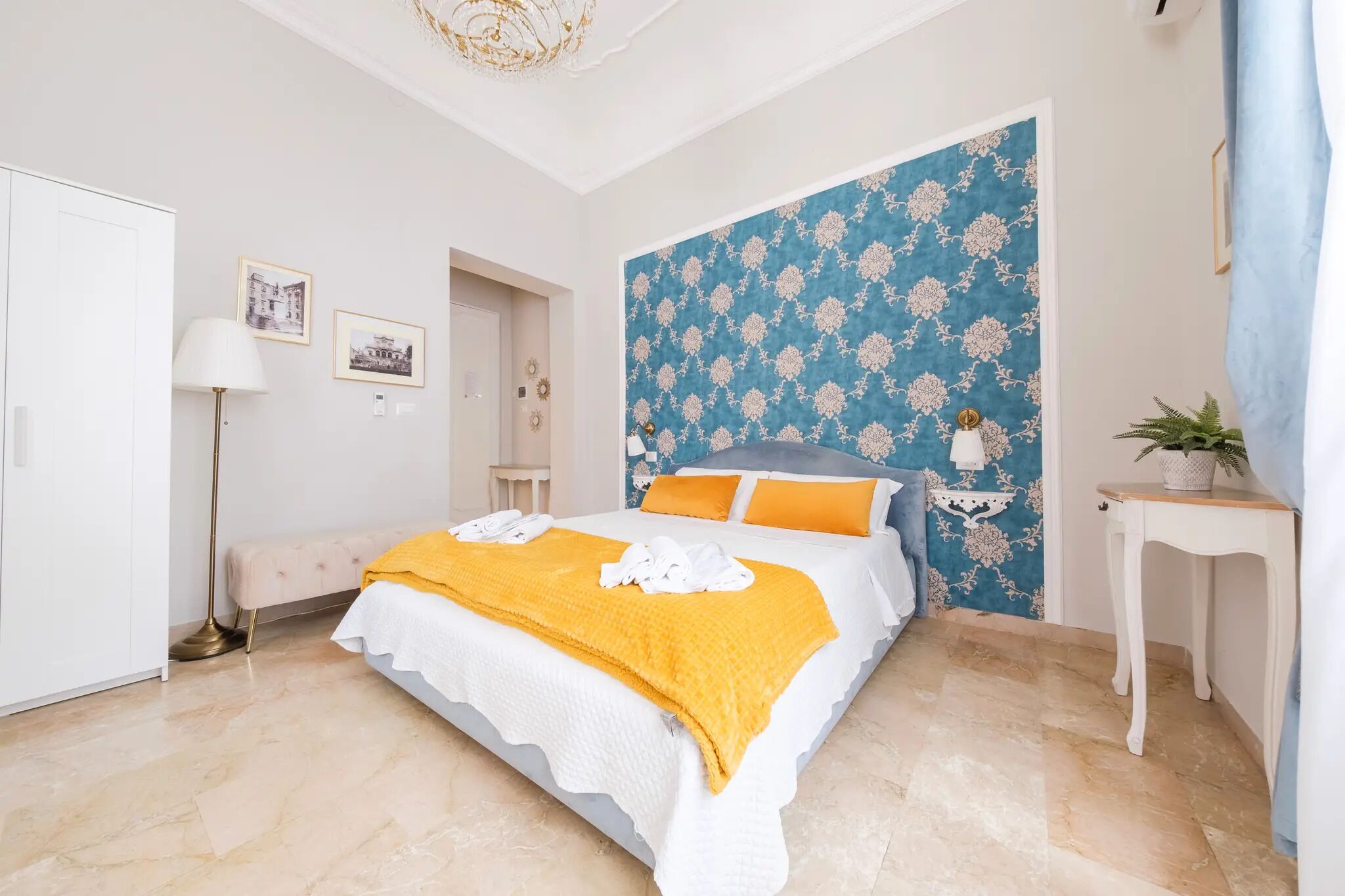 A bedroom with a bed, a bedside table, a lamp, and a wall with a floral pattern.