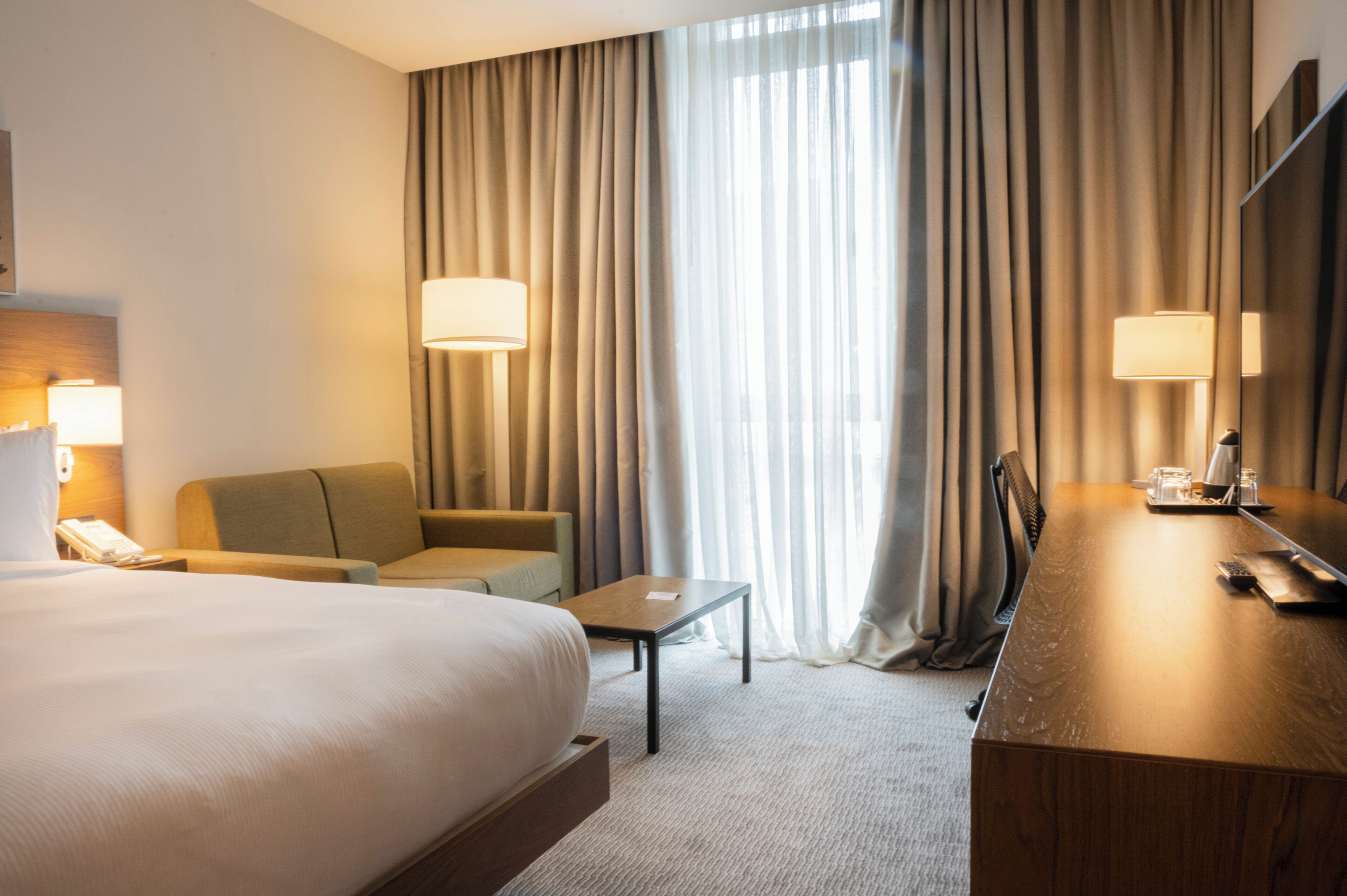 Una habitación de hotel con una cama grande, un escritorio, una silla, un sofá y una ventana con cortinas.