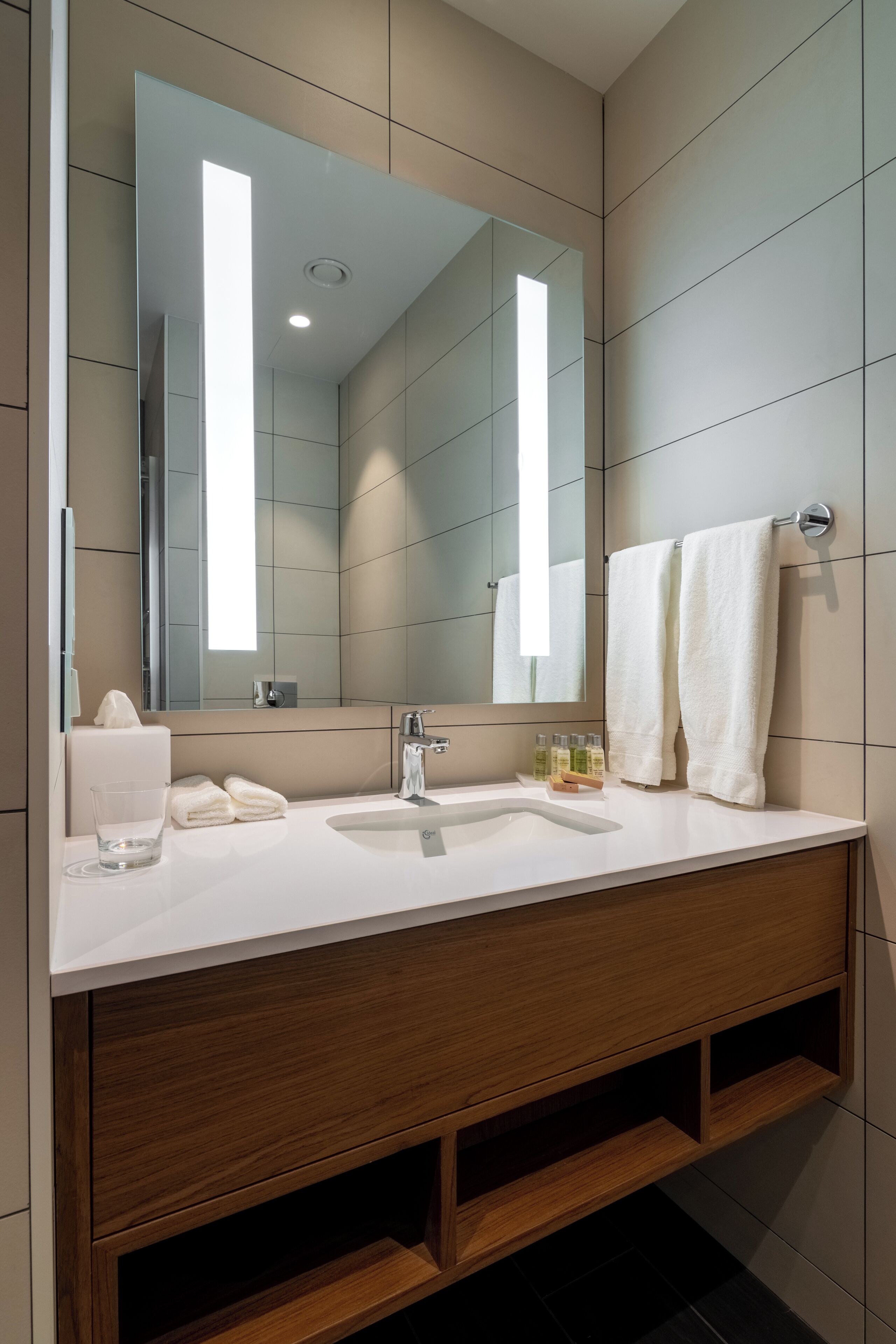 A modern bathroom with a large mirror, white sink, and wooden vanity.