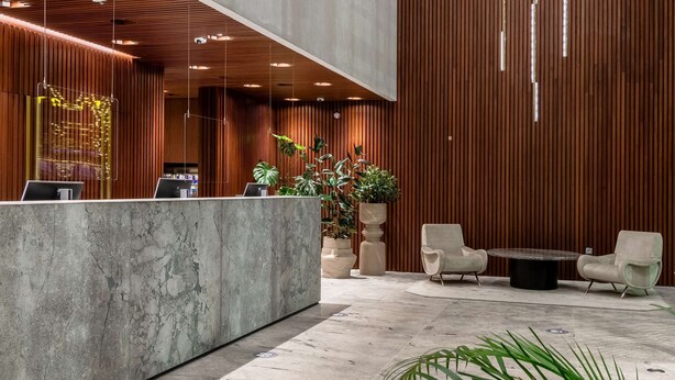 Una moderna recepción con mostrador de mármol, paneles de madera y una zona de estar con dos sillones y una mesa.