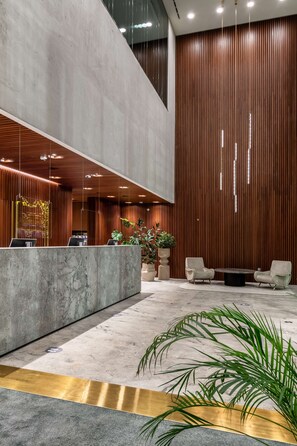 A modern reception area with a marble counter, wooden paneling, and a seating area with two chairs and a table. - Hilton Garden Inn Tbilisi Chavchavadze (Tbilisi)