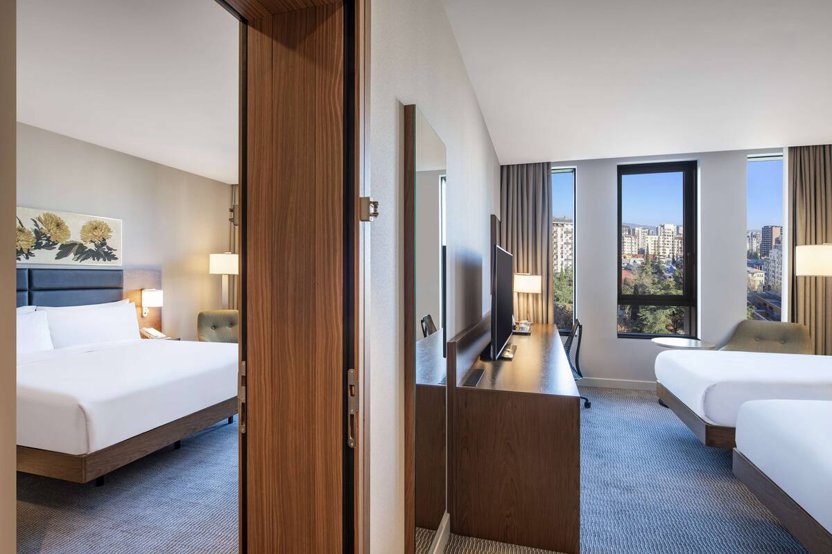 Hotelkamer met twee bedden, een bureau, een televisie en een groot raam met uitzicht op de stad.