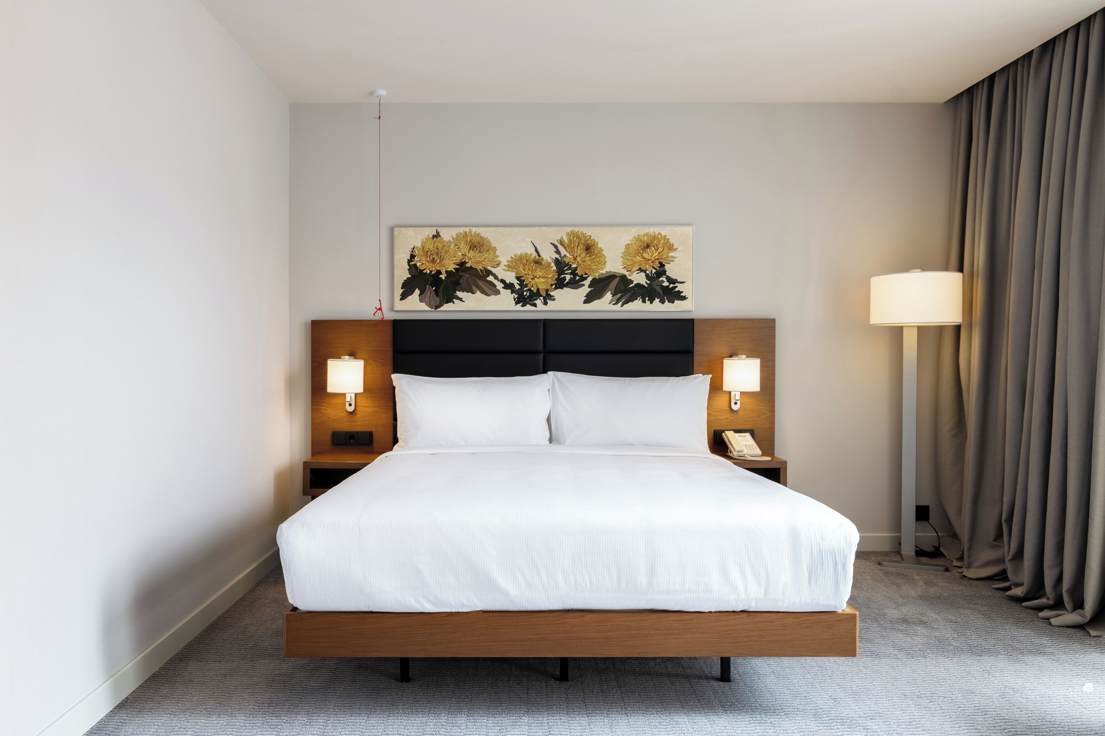 Ein Hotelzimmer mit einem großen Bett, zwei Nachttischen mit Lampen, einem Kopfteil und einem Gemälde darüber.