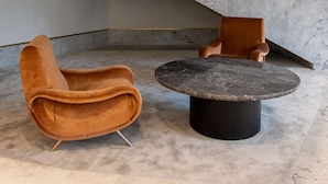Un interior moderno con suelo de mármol, una mesa redonda y dos sillas marrones.