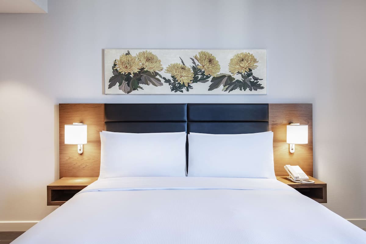 Een hotelkamer met een groot bed, twee nachtkastjes met lampen en een bloemstill leven aan de wand.