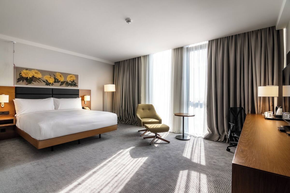 Een hotelkamer met een bed, bureau, stoel, lamp en een schilderij aan de muur.