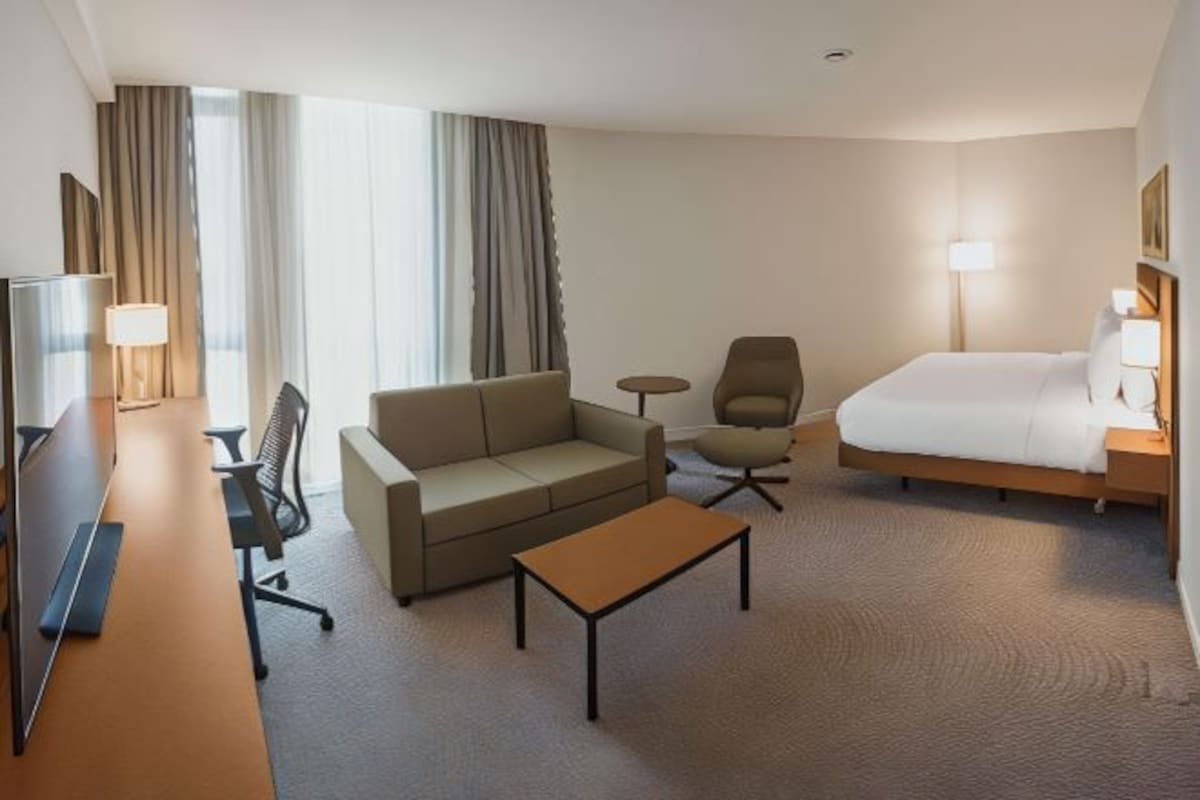 A hotel room with a bed, a sofa, a small table, a TV, and a lamp.