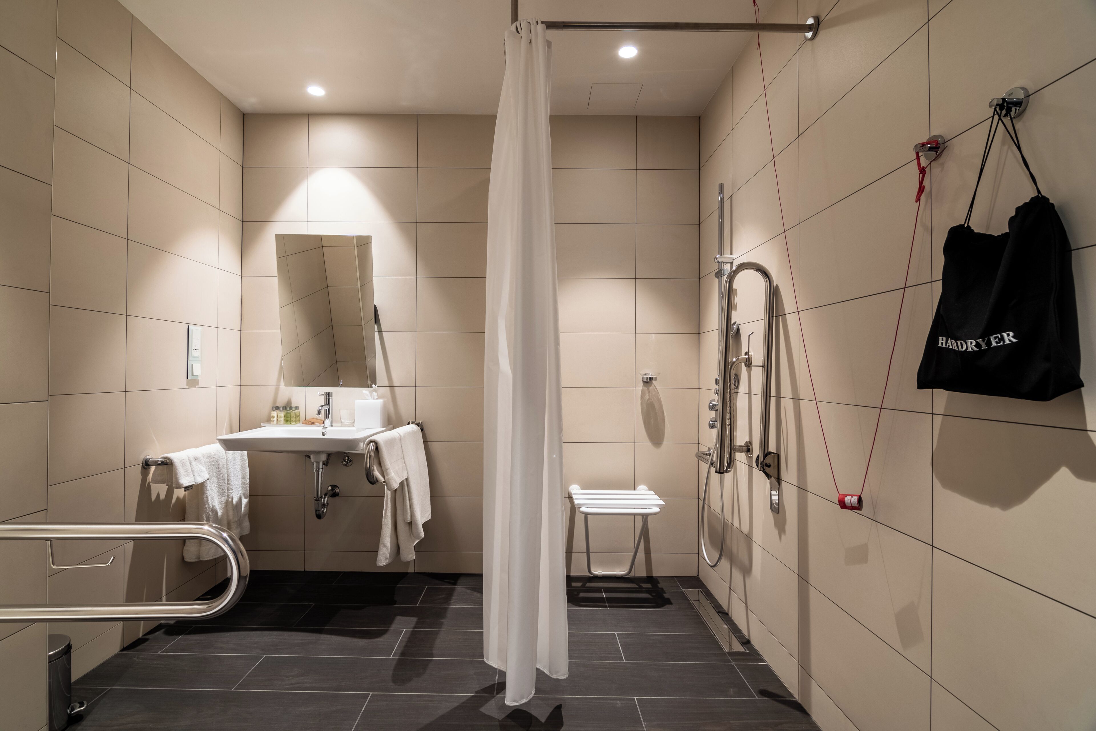 A modern bathroom with a shower, toilet, sink, and a towel rack with a bag.